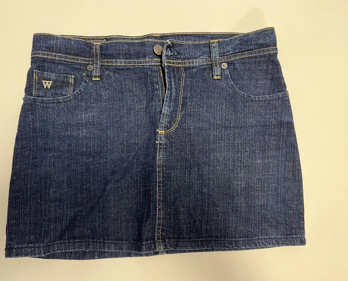 Minifalda de jean azul oscuro WANAMA, algo elastizado el Jean, con detalles de costuras amarillas y el logo de la marca "W" en el bolsillo. Ideal para un look casual y moderno.