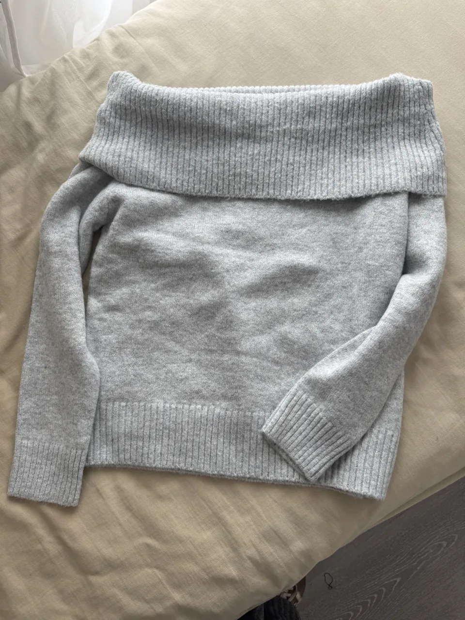Sweater gris de cuello ancho, con mangas largas y puños.