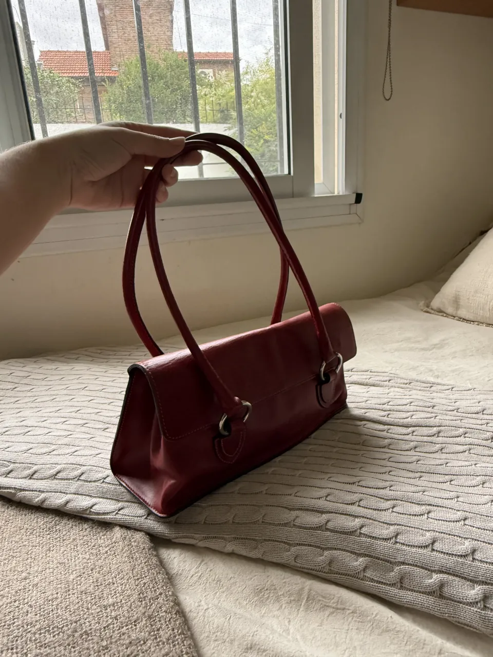 Cartera de cuero color rojo “shoulder bag” con manijas cortas y detalles metálicos plateados. Cierre de solapa.
