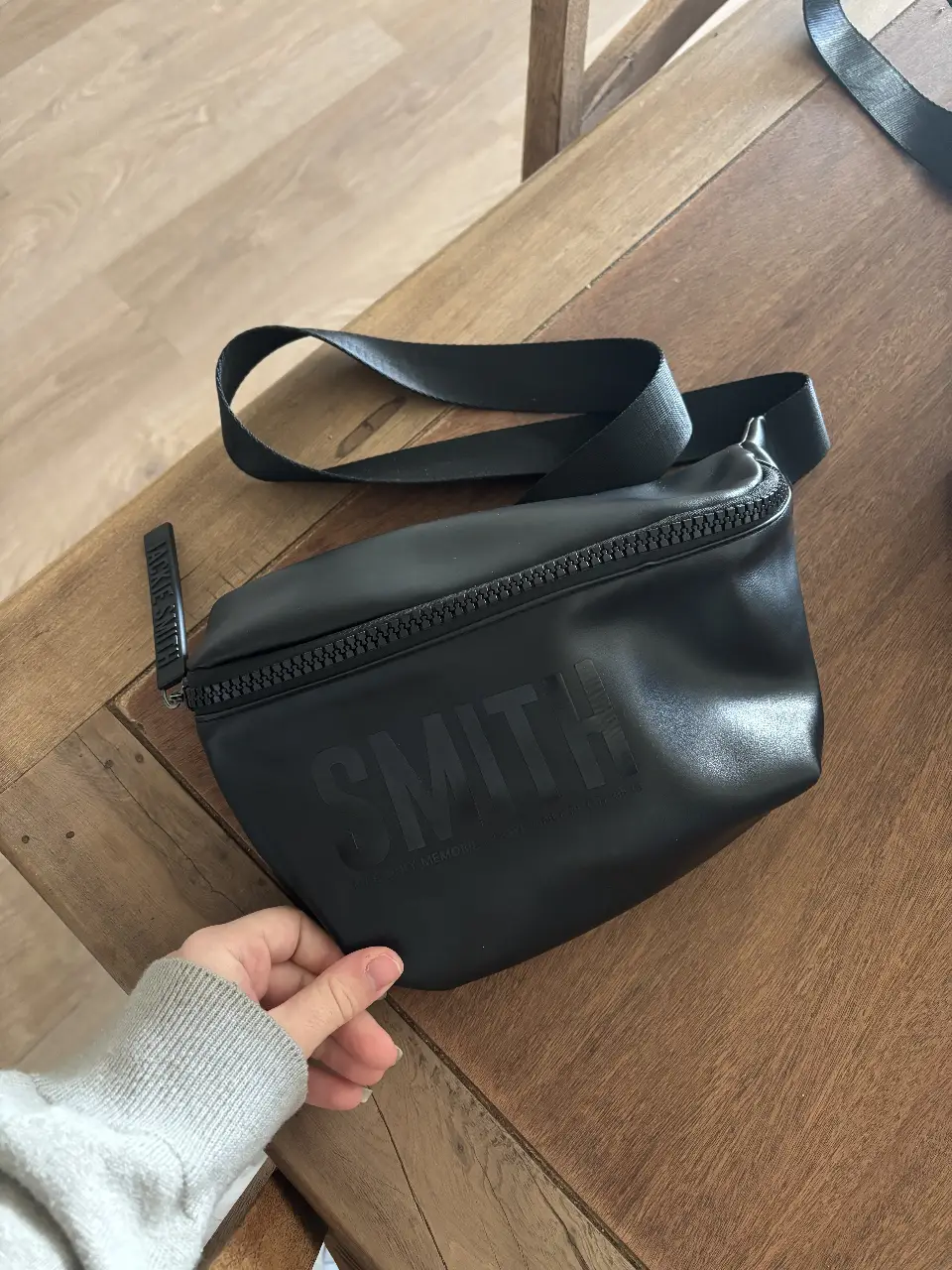 Riñonera Smith negra, ideal para llevar tus esenciales con estilo. Confeccionada en material resistente, cuenta con un compartimento principal amplio y un bolsillo interno. Perfecta para un look casual y moderno.