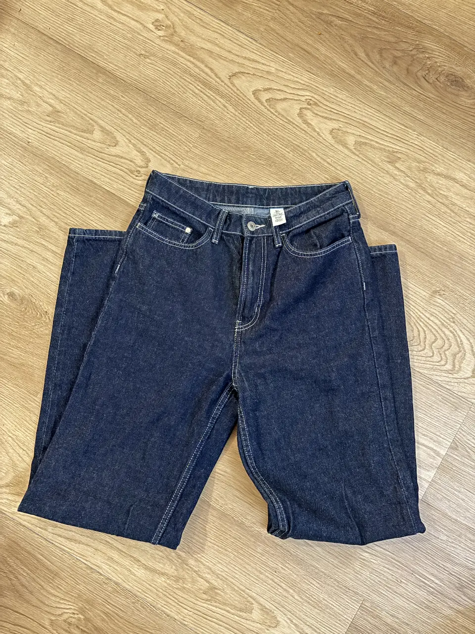 Jeans rectos de denim azul oscuro, tiro medio, con costuras blancas en contraste. Un clásico atemporal para cualquier guardarropa.