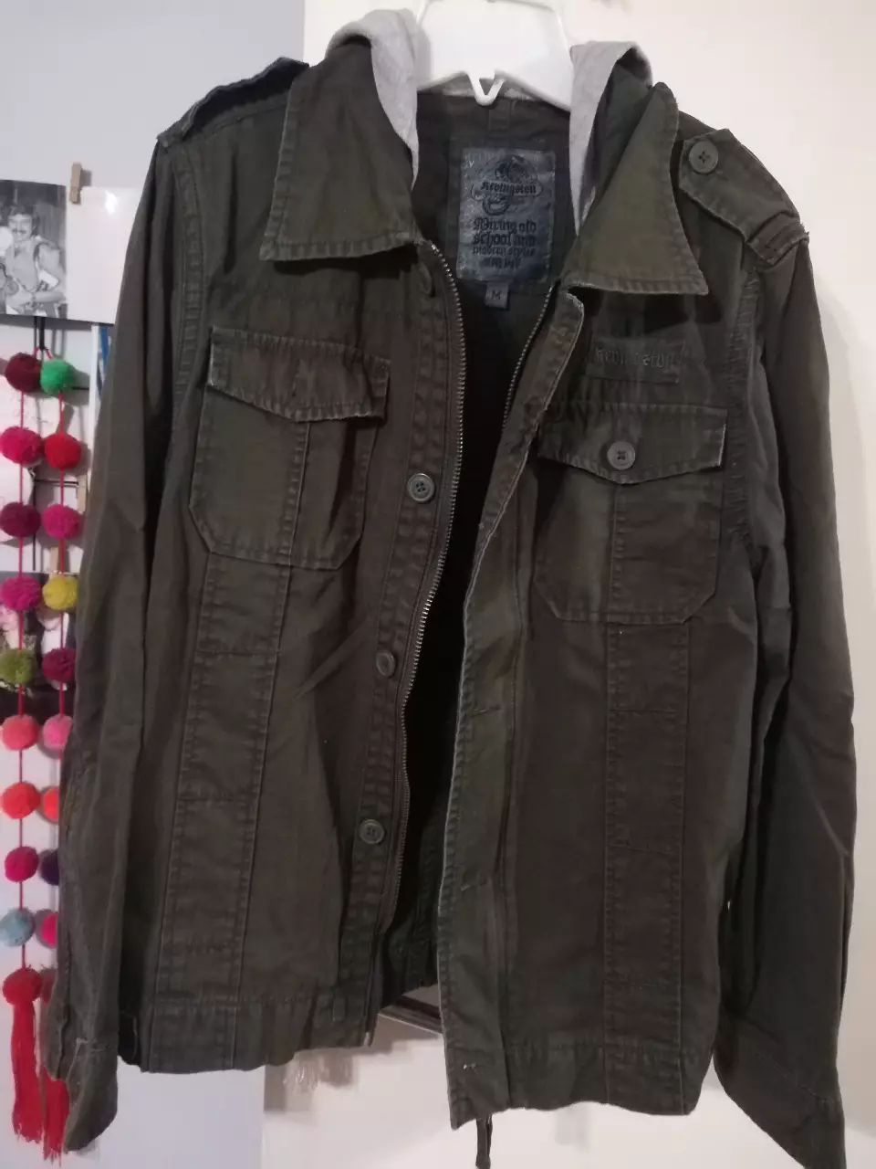 Campera tipo bomber de hombre, color verde oscuro con capucha gris. Posee cierre y bolsillos delanteros. Ideal para un look casual y urbano.