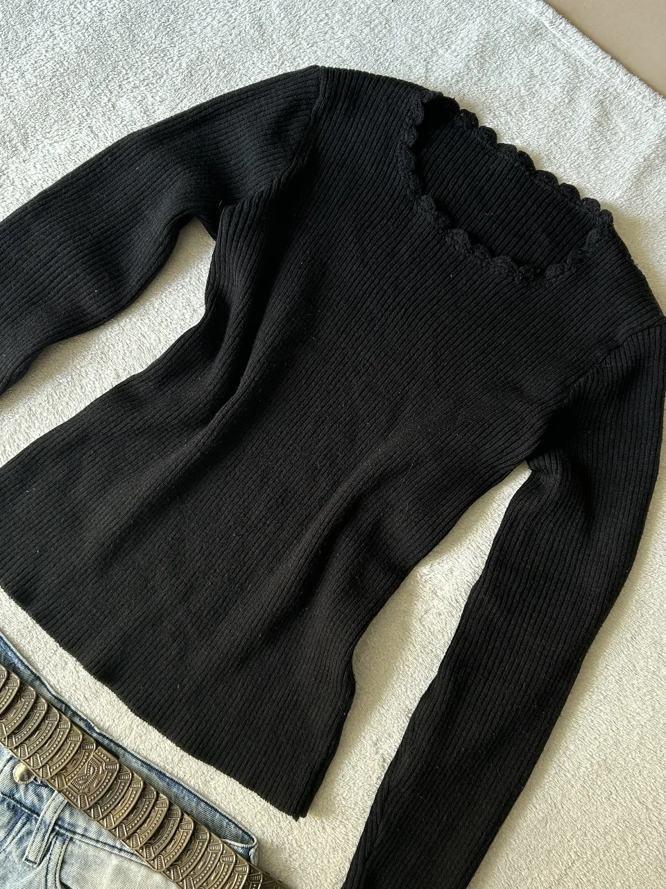 Sweater negro de manga larga con cuello escote en V y detalle de ondas en el borde. Tejido acanalado que se ajusta al cuerpo, ideal para un look canchero y elegante.