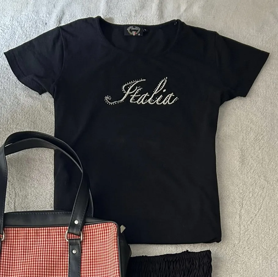 Remera negra con la palabra "Italia" bordada en pedrería plateada. Un diseño sutil y elegante, perfecto para un look casual chic.