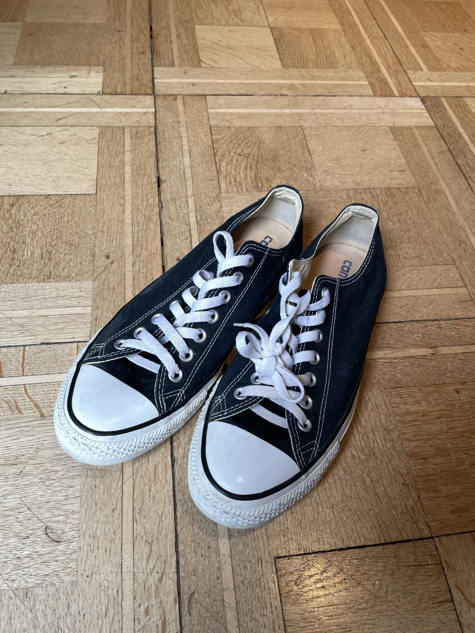 Zapatillas CONVERSE bajas de lona negras con cordones blancos y puntera reforzada blanca.