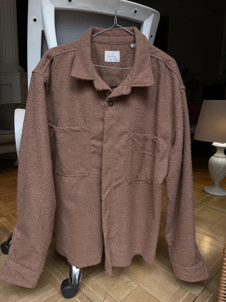 Camisa de manga larga de color marrón. Posee dos bolsillos en la parte delantera y un botón en el cuello.