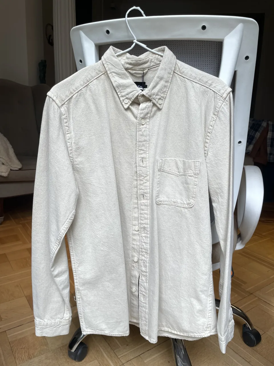 Camisa de manga larga color crudo con cuello. Posee un bolsillo en el frente izquierdo y botones en la parte delantera y en los puños.