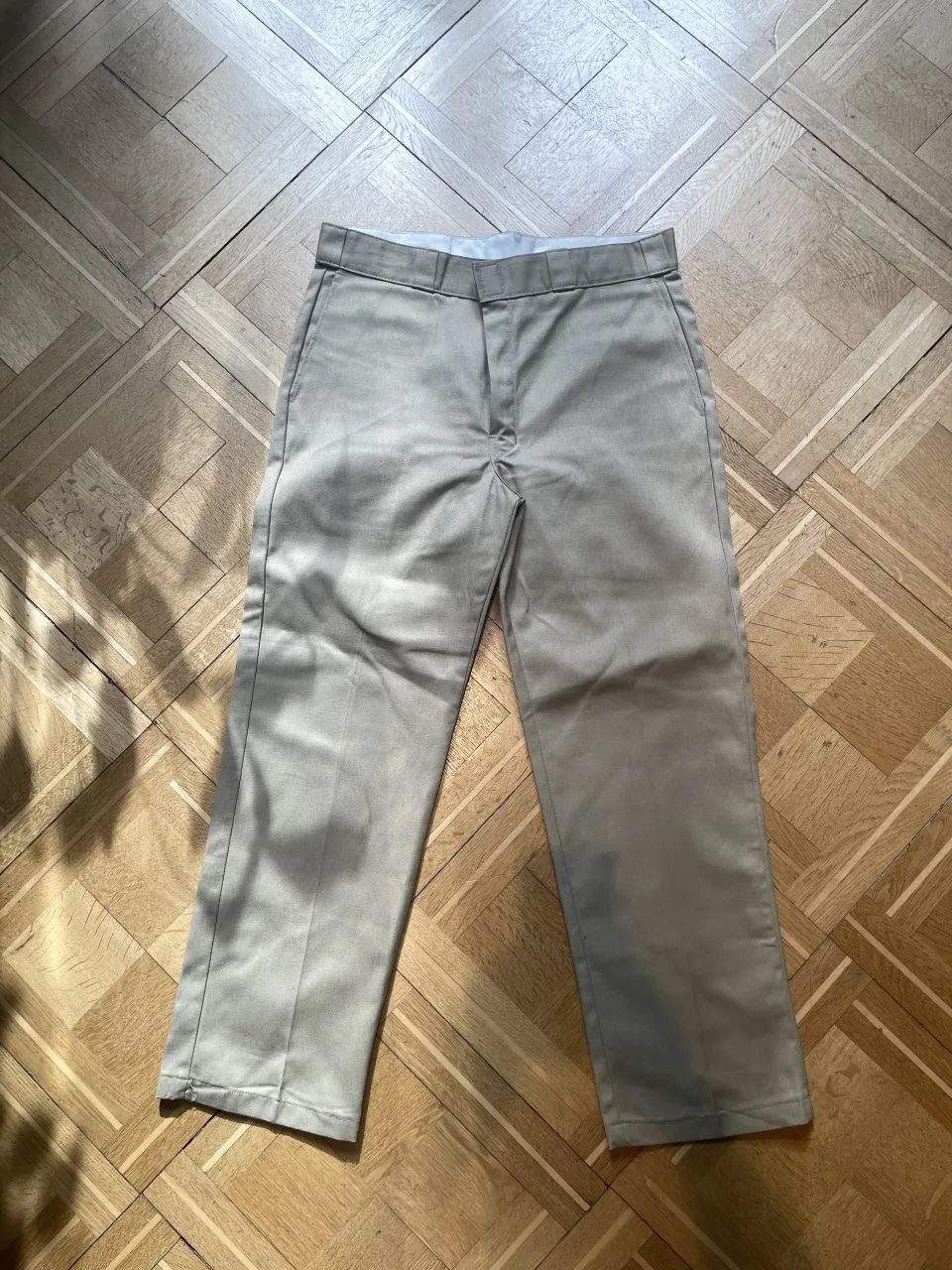 Pantalón de gabardina color beige. Tiene bolsillos delanteros y traseros. Posee un pequeño logo de la marca en el bolsillo trasero derecho.