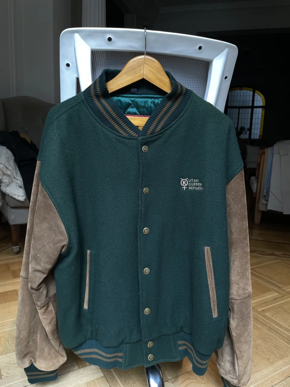 Campera estilo universitaria, color verde con mangas y detalles en marrón. Posee botones al frente y logo bordado en el pecho.