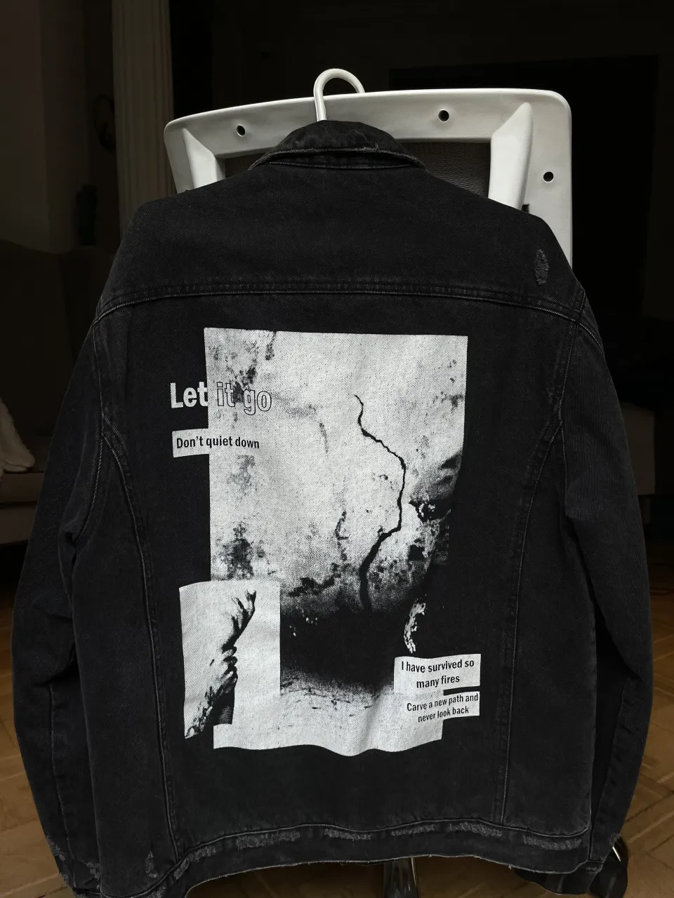 Campera de jean negra BERSHKA con detalles de roturas y estampas. En la espalda tiene una estampa grande con texto y una imagen abstracta. En el frente, sobre el bolsillo izquierdo, tiene un texto estampado.