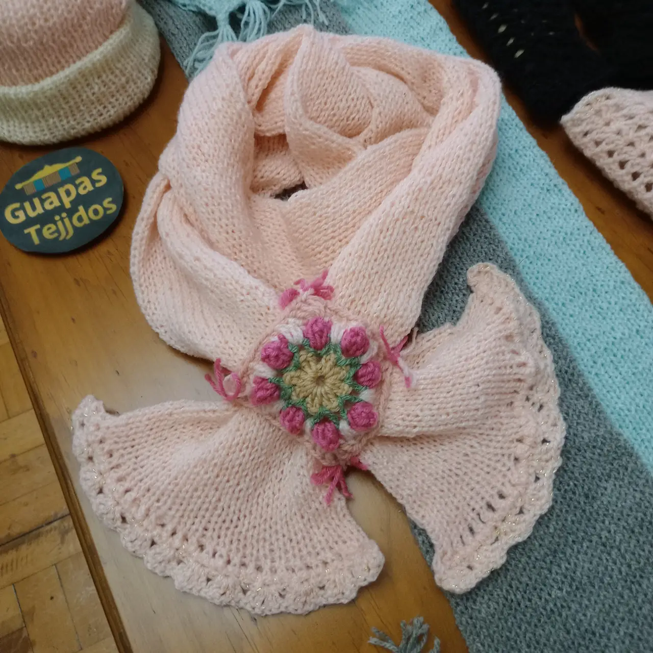 Bufanda tejida a mano en color rosa (podes pedir en cualquier color, celeste , gris , etc) con detalle floral en el centro y bordes con volados. Ideal para complementar cualquier look de invierno.