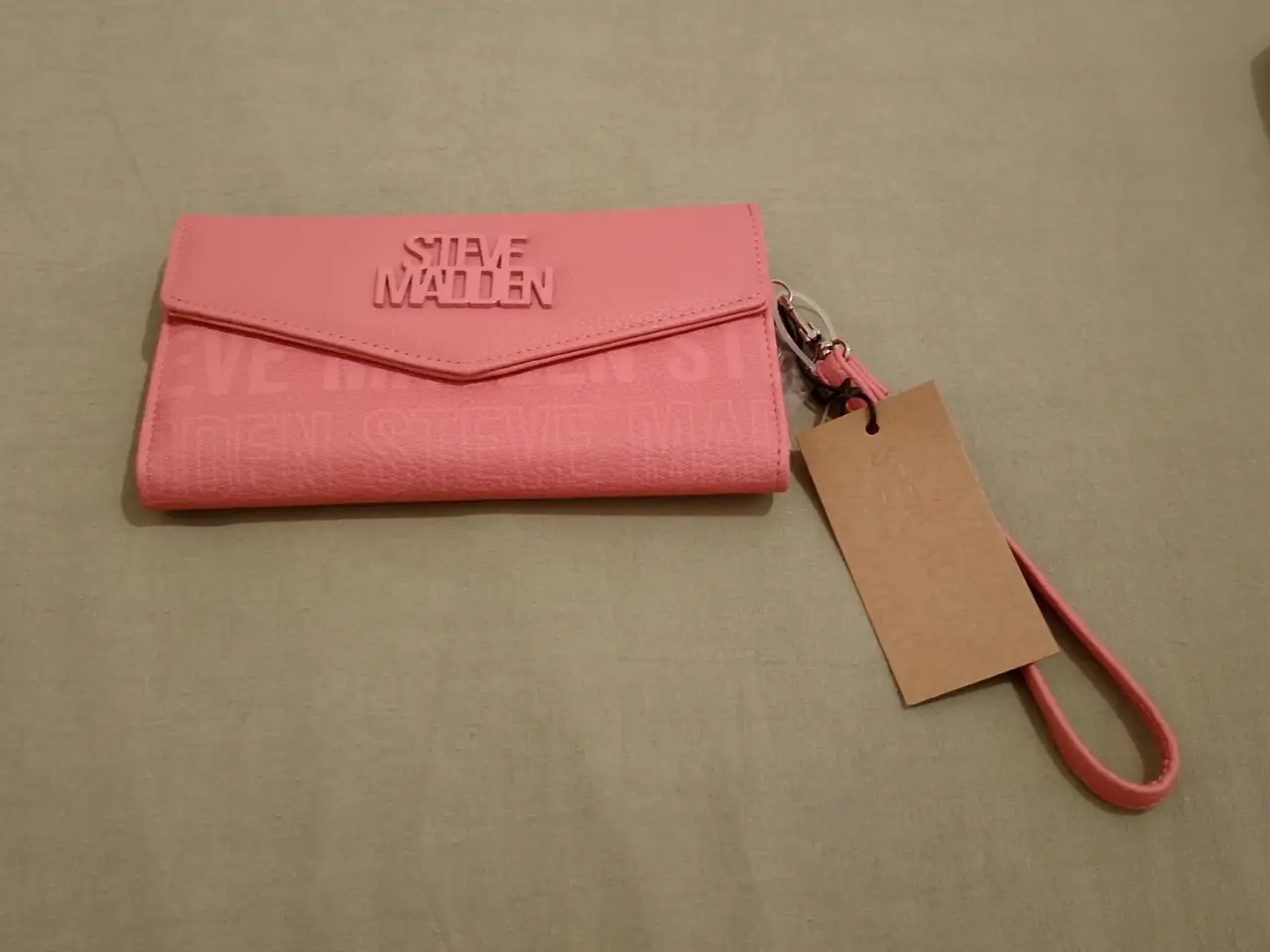 Billetera rosa de la marca Steve Madden, con cierre y correa para la muñeca. Ideal para llevar tus esenciales con estilo.