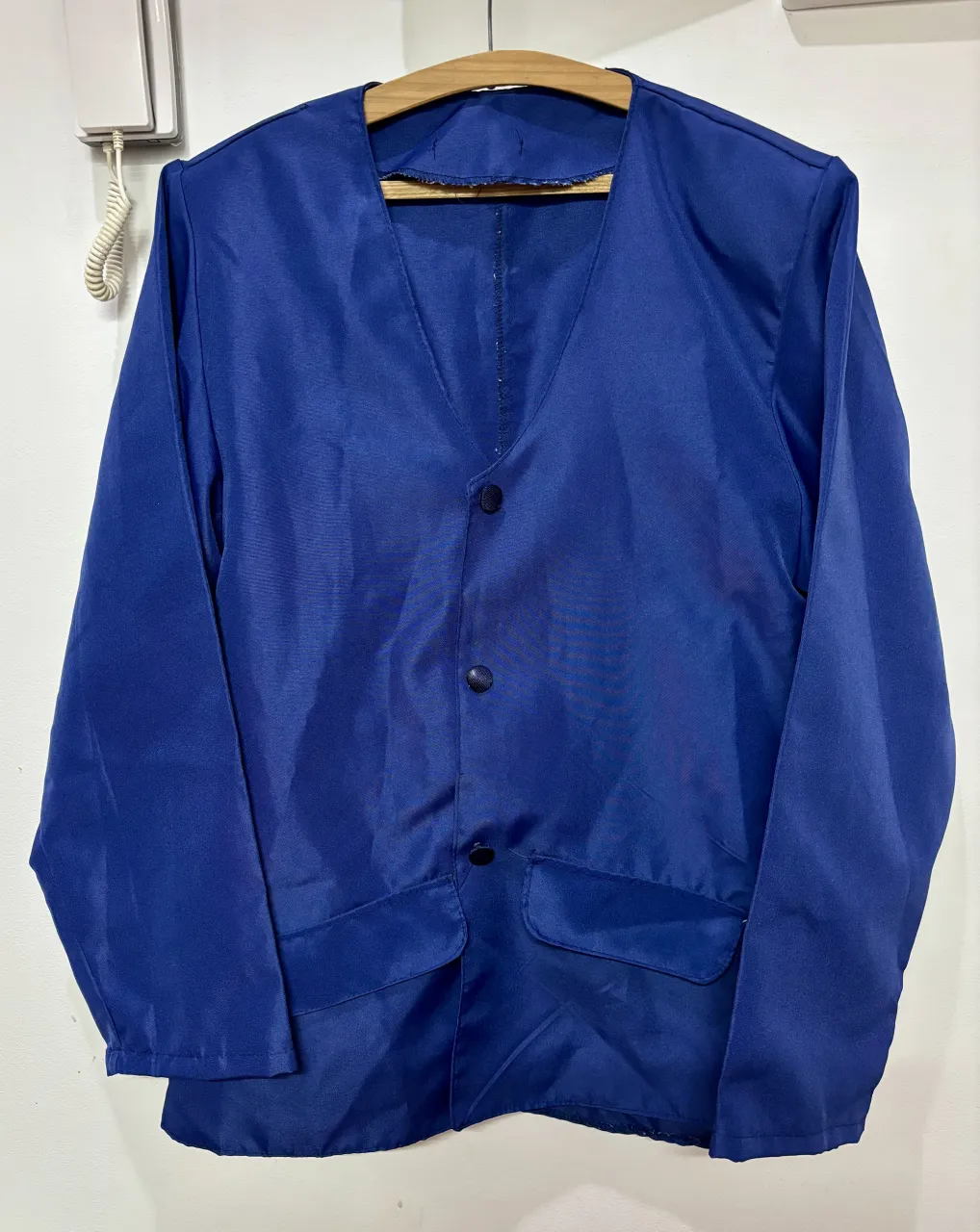 Blusa tipo chaqueta color azul con cuello en V y tres botones al frente. Posee dos bolsillos inferiores con solapa.