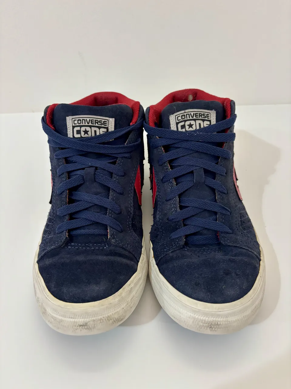 Zapatillas Converse altas de gamuza azul marino con detalles en rojo. Cierre de cordones y suela blanca.