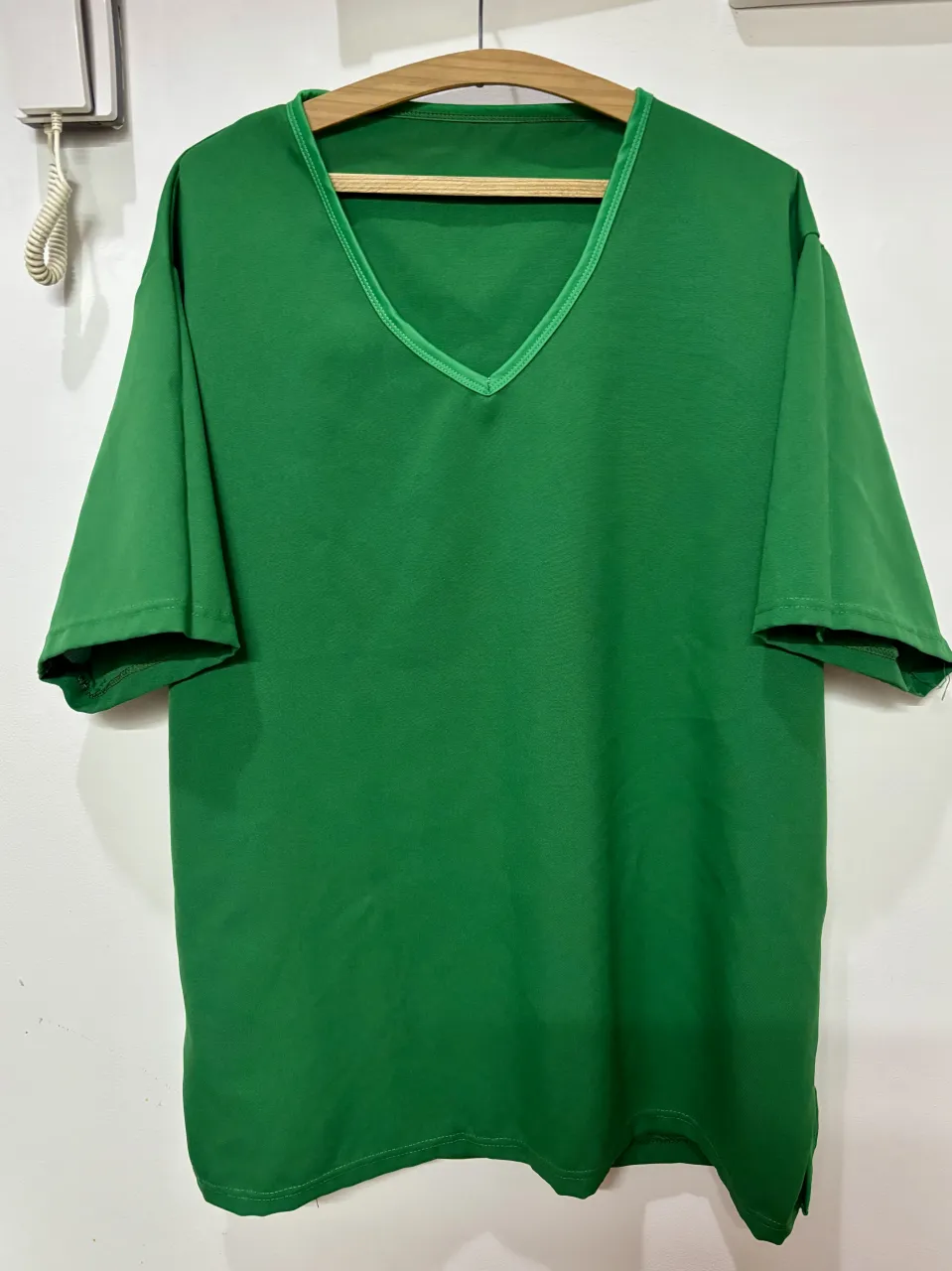 Remera verde con cuello en V y detalles en el borde del cuello. Posee aberturas laterales en la parte inferior.