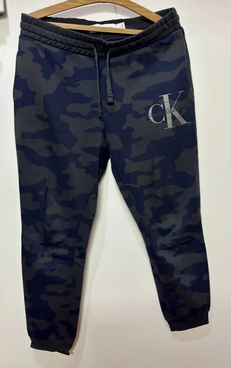 Pantalón de jogging con estampa camuflada en tonos azules y grises. Posee logo de Calvin Klein Jeans estampado en el frente. Cintura con cordón.