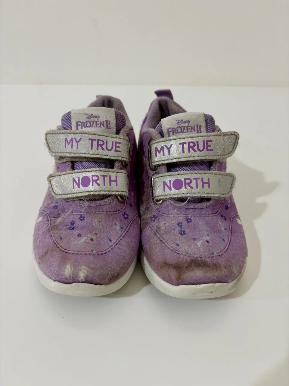 Zapatillas de niña color lila con temática de Frozen II. Tienen dos abrojos plateados con la inscripción "MY TRUE NORTH". Presentan estampas de flores y personajes de la película.
