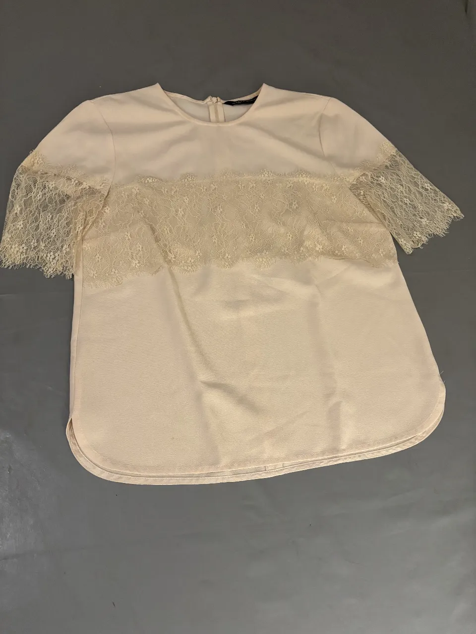 Blusa de mujer color crudo con detalles de encaje en el frente y mangas cortas. Ideal para un look elegante y femenino.
