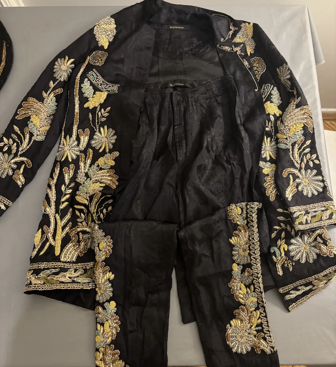 Conjunto de dos piezas negro con bordados dorados. Incluye chaqueta con detalles florales y pantalón a juego.