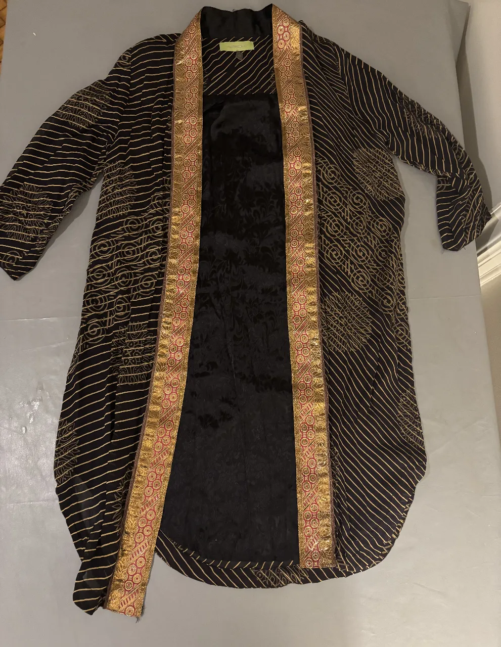 Kimono largo de mujer en color negro con detalles dorados. Posee un diseño con estampado y bordes dorados y rojos. Ideal para un look elegante y sofisticado.