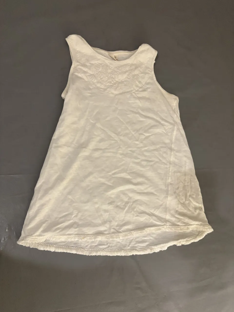 Musculosa blanca con detalles bordados en el pecho y flecos en el borde inferior. Ideal para un look fresco y casual.