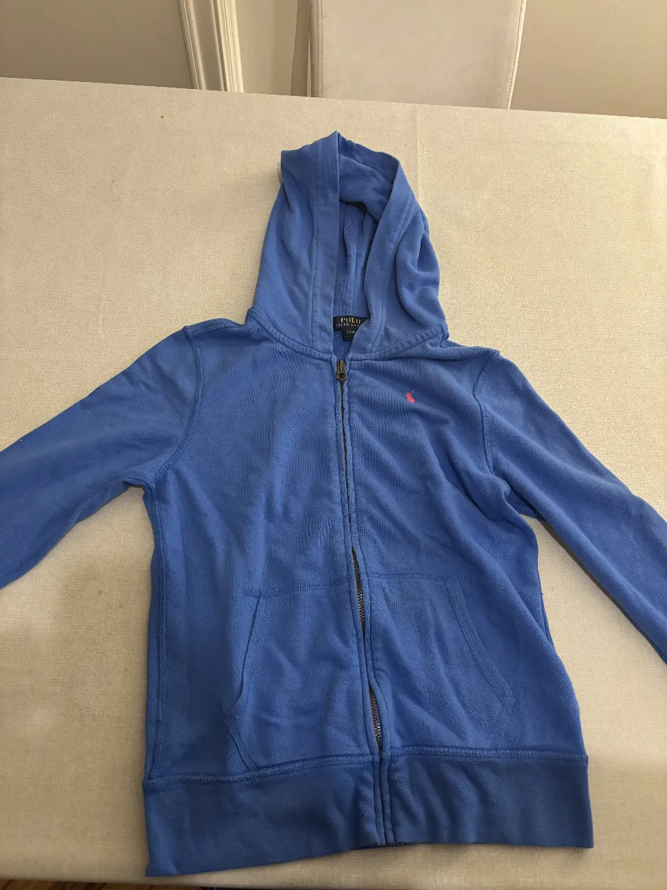 Buzo azul con capucha y cierre completo. Tiene bolsillos tipo canguro y el logo de la marca bordado en el pecho. No es muy abrigado. Ideal para un look casual y cómodo.