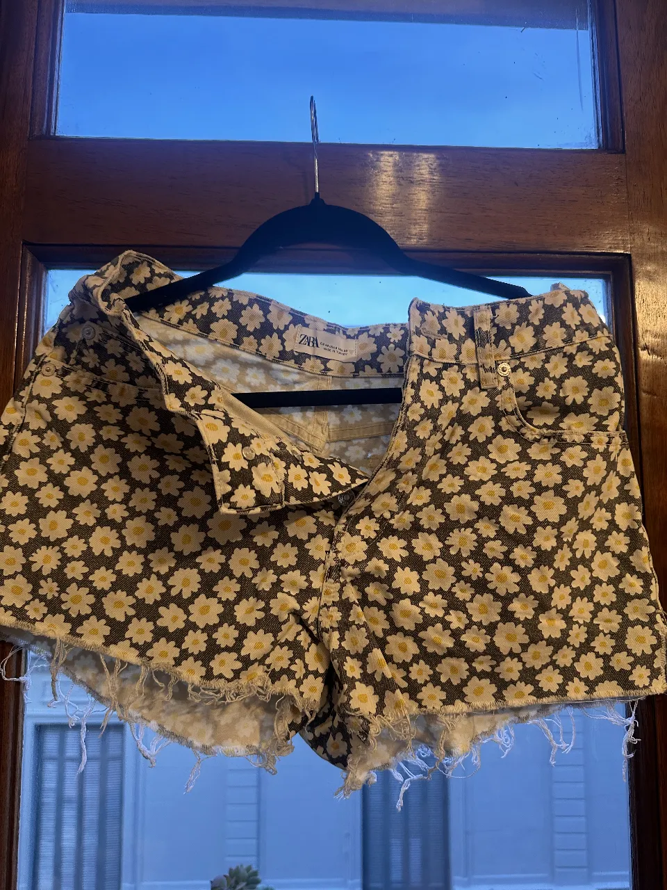 Short de jean de mujer con estampado de flores blancas sobre fondo negro. Tiro alto, con detalles de roturas en los bordes. Ideal para un look casual y fresco.