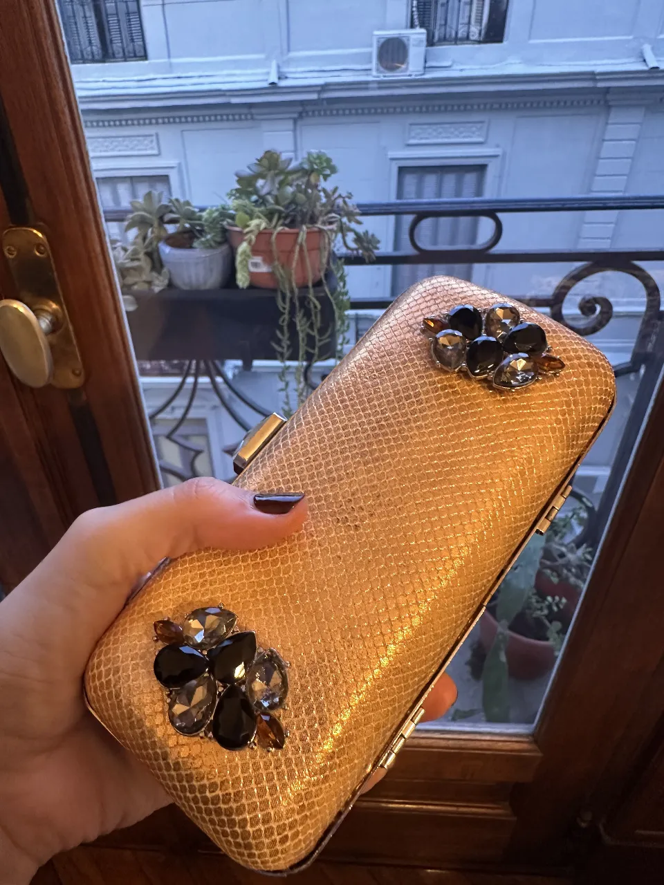 Cartera de mano dorada con detalles de piedras en tonos oscuros. Ideal para eventos y fiestas.