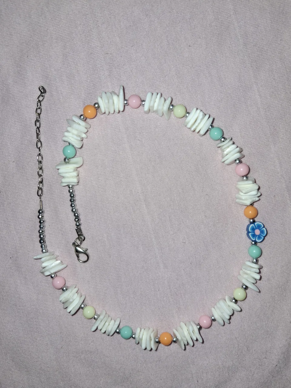 Collar de mostacillas blancas y de colores con un dije de flor azul.