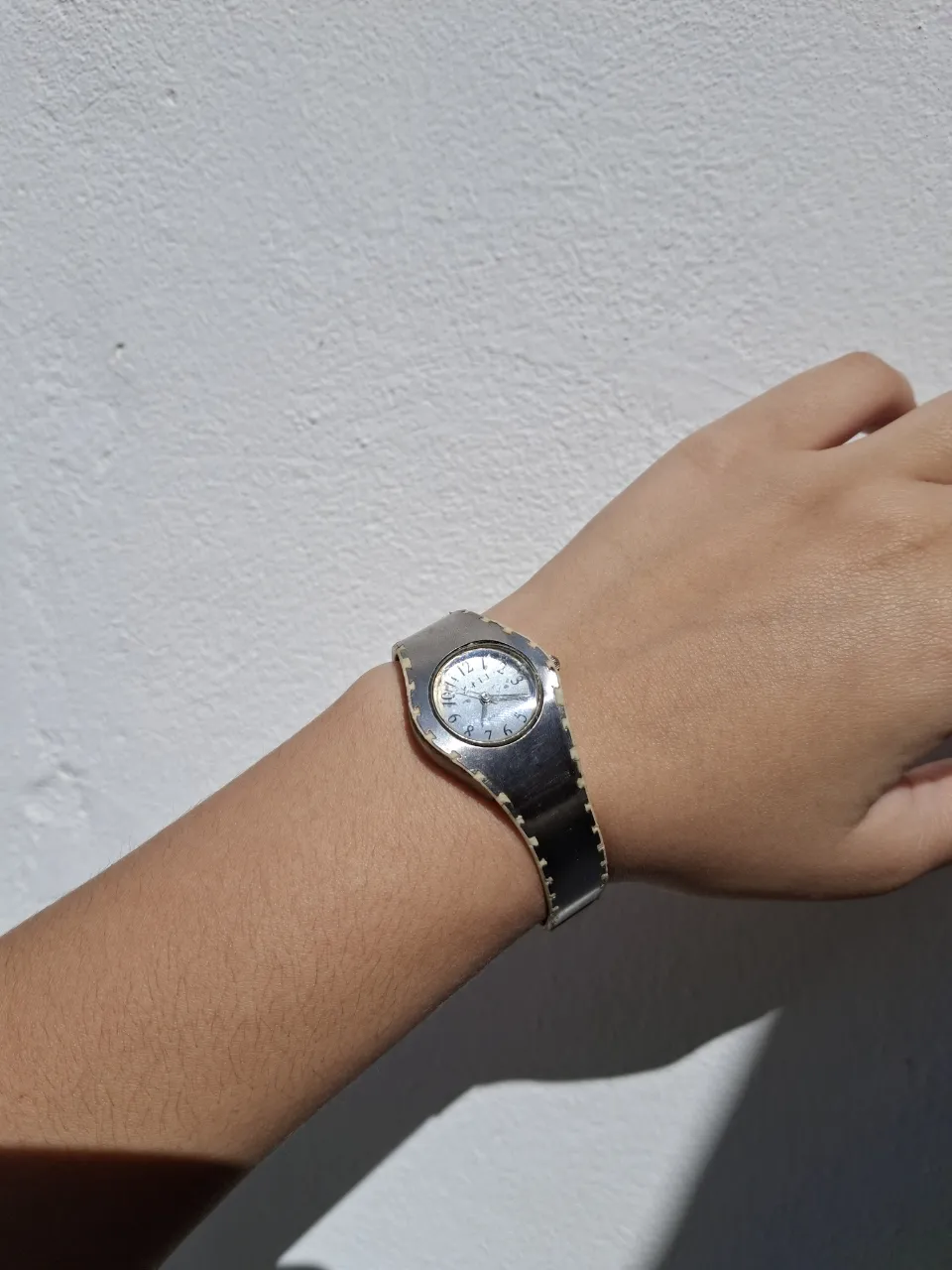 Reloj plateado con malla ancha y cuadrante redondo.