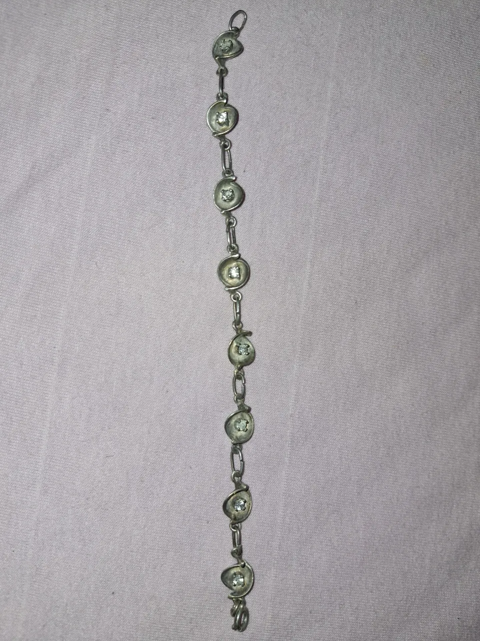 Pulsera de eslabones plateada con dijes redondos y piedras transparentes.