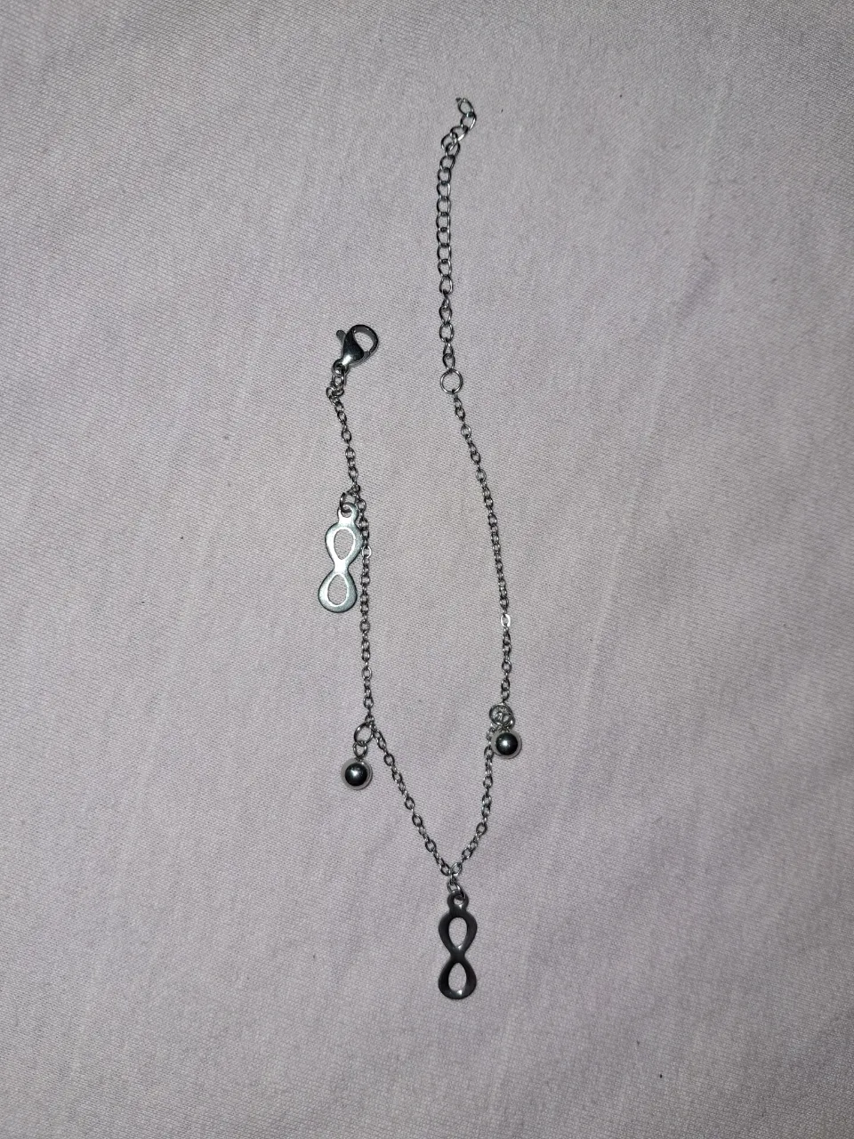 Tobillera de cadena plateada con dije de infinito y bolitas.