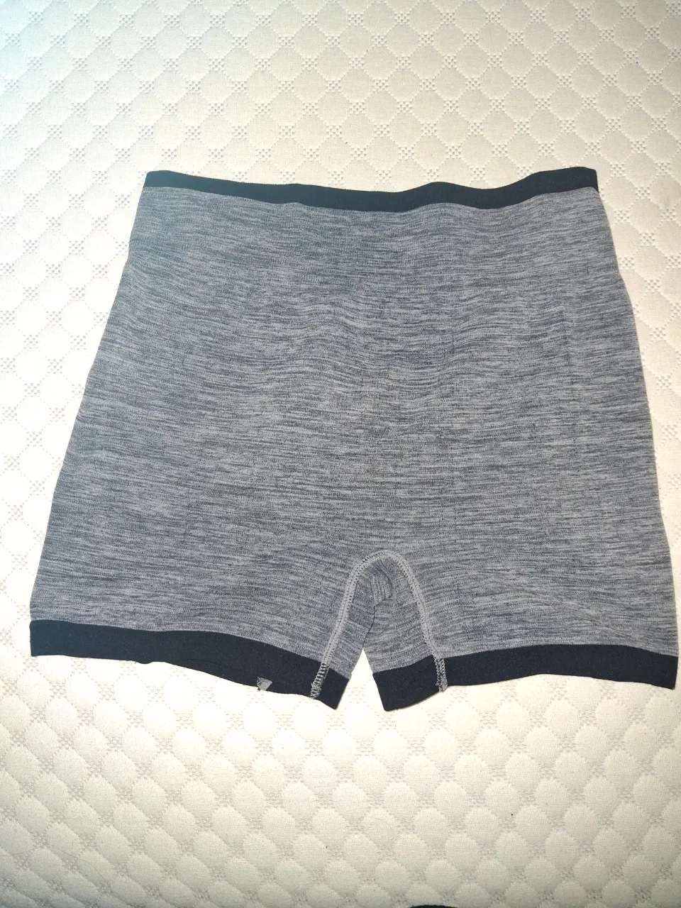 Shorts de tela gris jaspeada con detalles y elástico negro en cintura y borde inferior. Presenta un diseño fruncido en la parte trasera.