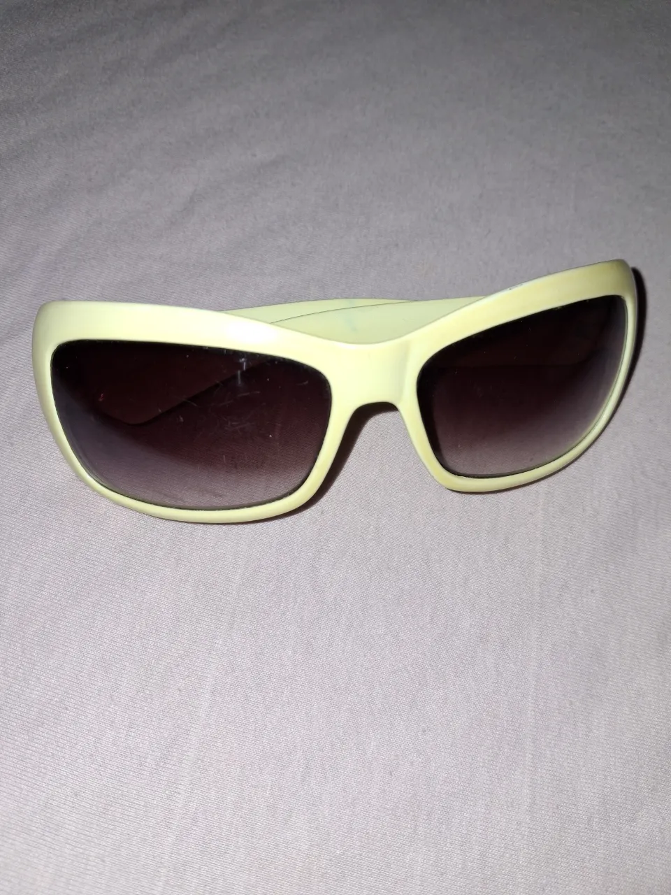 Anteojos de sol con armazón color amarillo pastel y lentes degradé en tonos marrones.