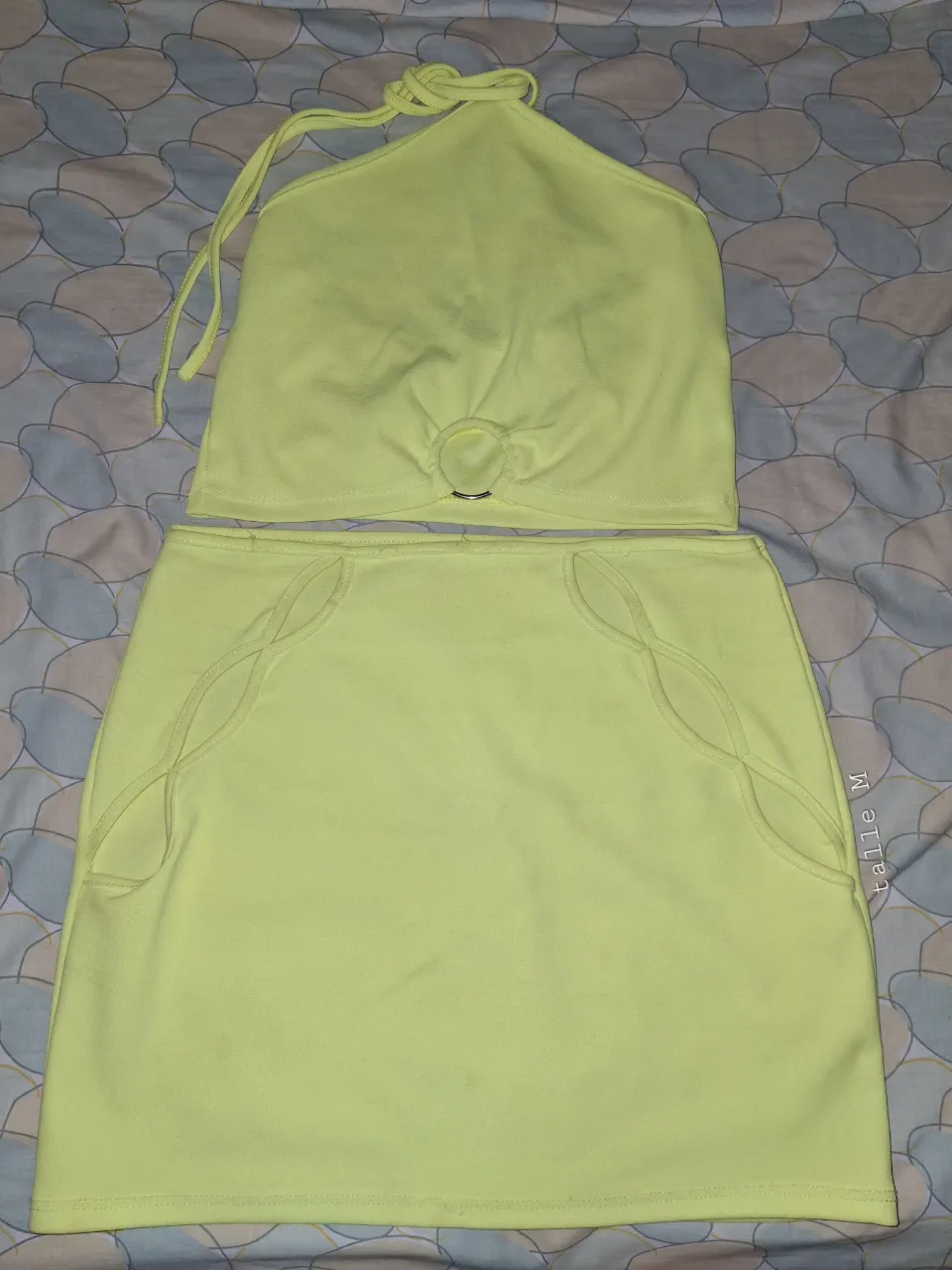 Conjunto de top y pollera color verde flúor. El top tiene tiras para atar en la nuca y detalle de aro metálico en el escote. La pollera es corta con detalles de recortes curvos en los laterales.