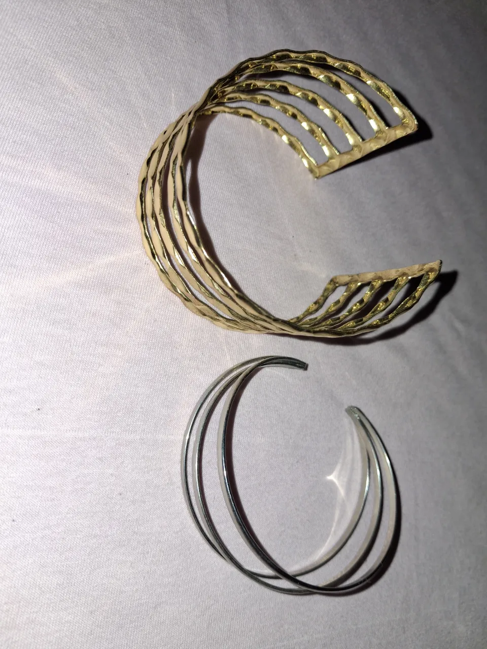 Set de dos pulseras. Una pulsera ancha dorada con diseño calado y otra pulsera fina plateada de tres aros entrelazados.