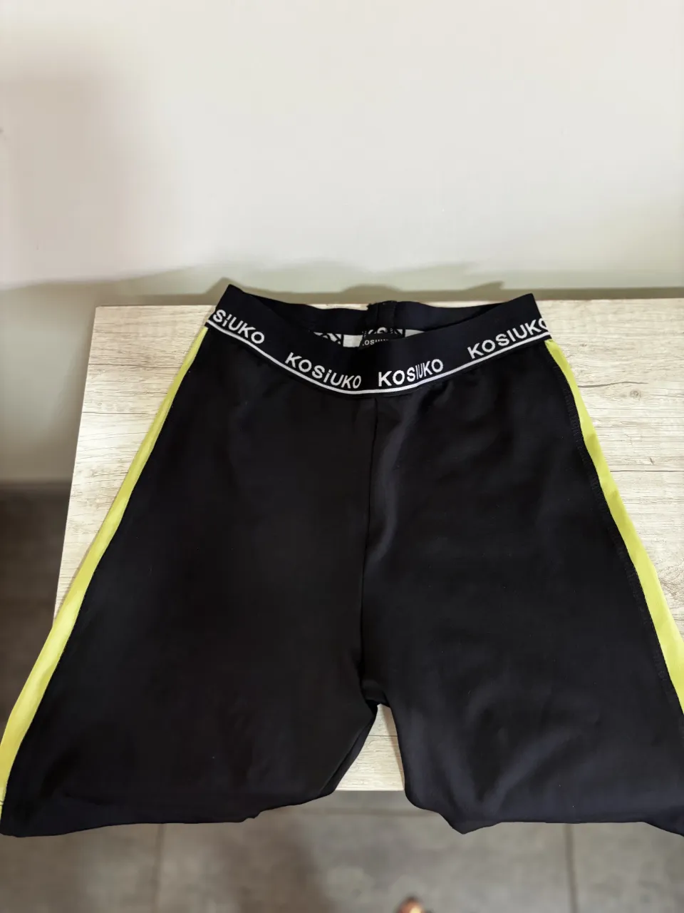 Shorts Kosiuko negros con cintura elastizada y detalles laterales en color amarillo flúo. La cintura tiene el logo de la marca repetido.