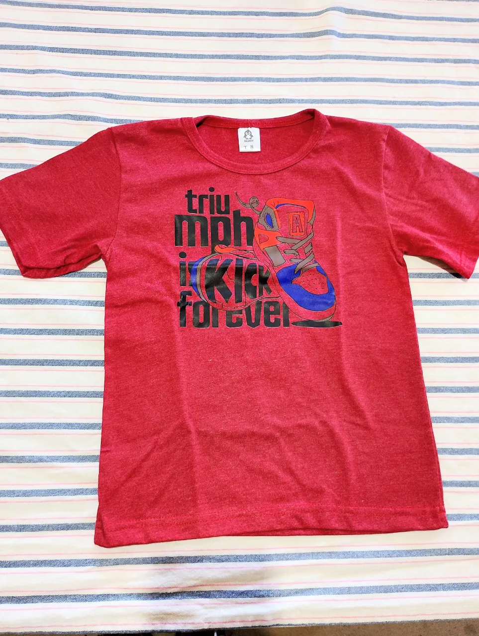 Remera de manga corta de color rojo con estampa de zapatillas y texto "triumph kick forever".