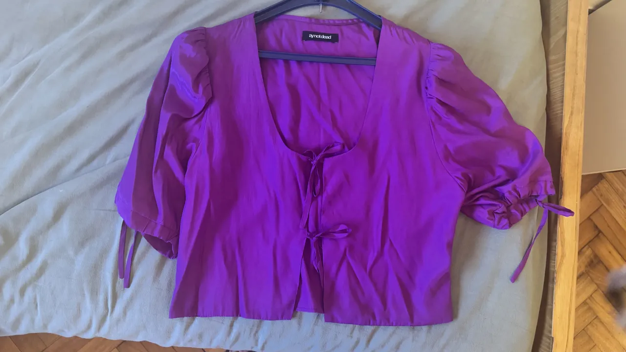 Blusa satinada súper linda y canchera, ideal para un look de día o de noche. Tiene mangas abullonadas con detalle de lazo en los puños y escote en V con amarre al frente. ¡Un toque súper femenino y a la moda!