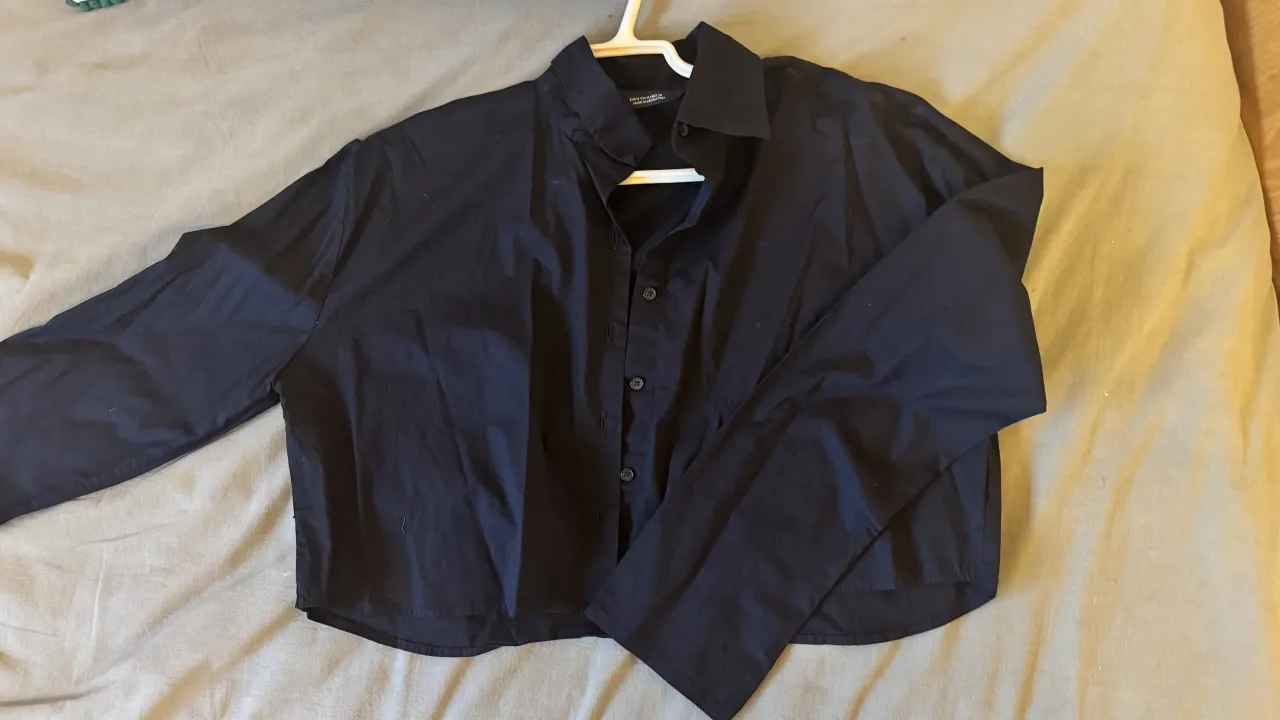 Camisa negra crop de manga larga, con botones al frente y cuello clásico. Un básico versátil para cualquier look.