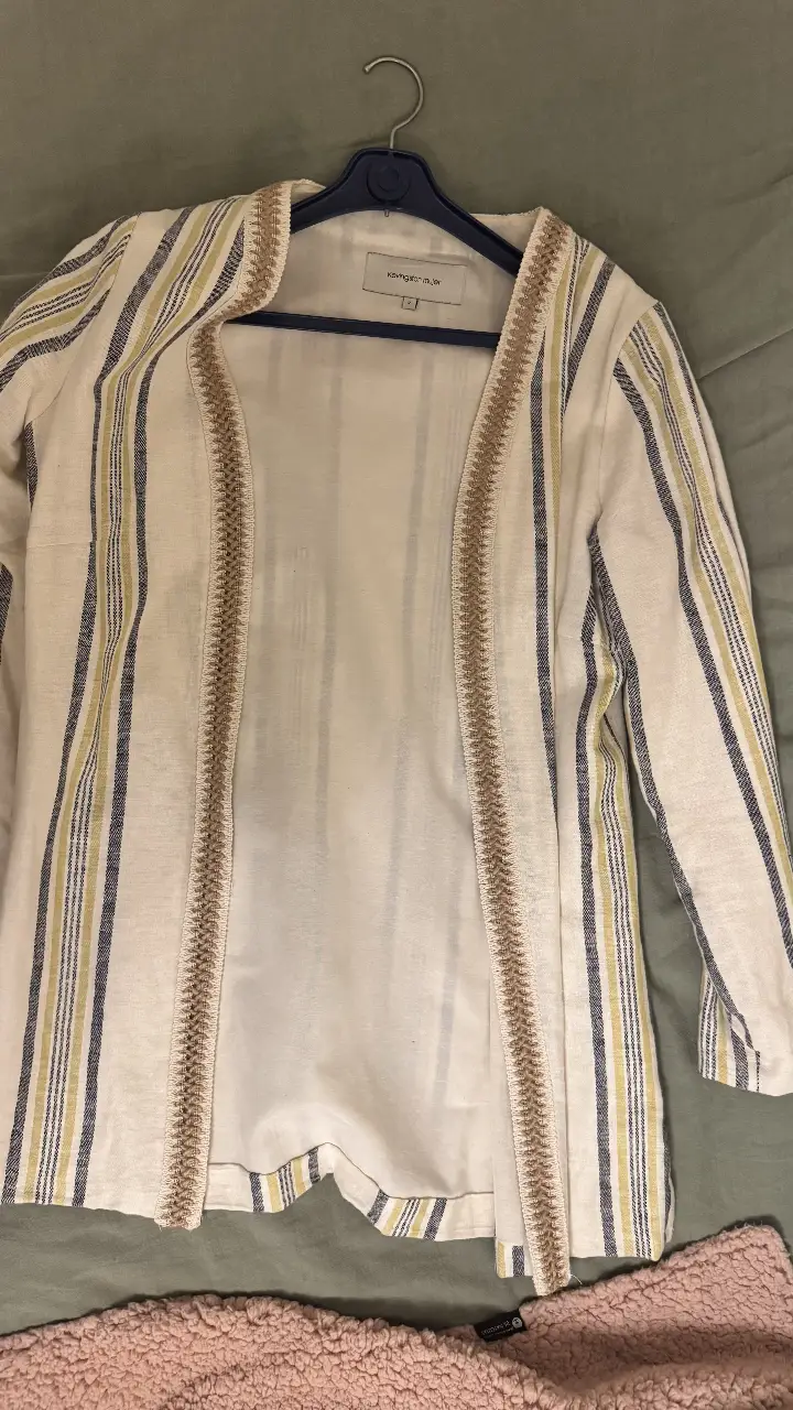 blazer lino con rayas verticales en blanco, amarillo y azul. Detalles de bordado en los bordes y cuello. Ideal para un look casual y fresco.