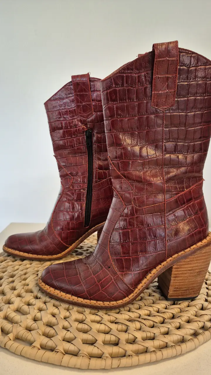 Botas de caña alta de cuero con diseño de cocodrilo en color borgoña. Tienen cierre lateral y taco ancho de madera.