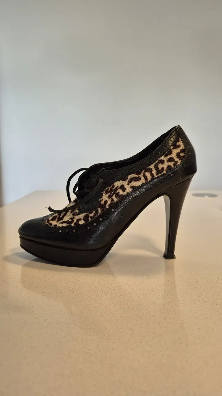 Zapatos de taco alto de cuero negro con detalles de estampado de leopardo en la parte superior. Diseño de cordones y plataforma.