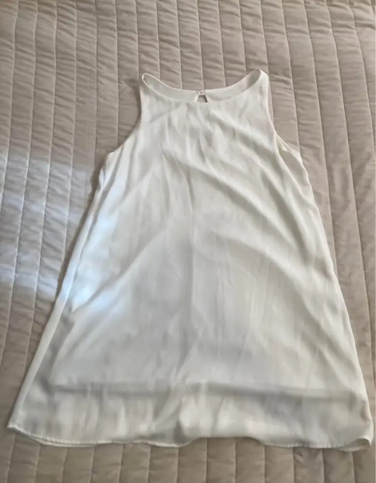 Vestido blanco corto forrado sin mangas, con cuello redondo y detalle de abertura en la espalda. Ideal para un look fresco y elegante.