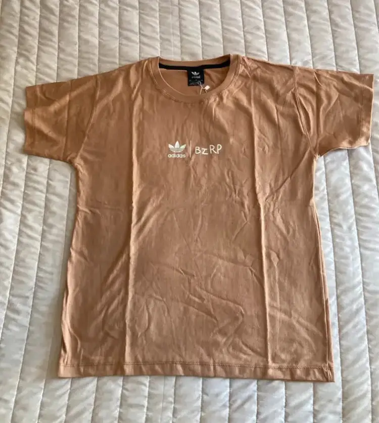 Remera Adidas BzRP, de color marrón claro, con el logo de Adidas y la inscripción BzRP en blanco. Ideal para un look deportivo y casual.