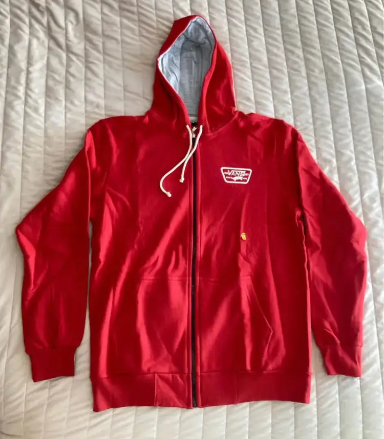 Buzo canguro con cierre y capucha, de la marca Vans. Color rojo con detalles en gris. Ideal para un look casual y urbano.