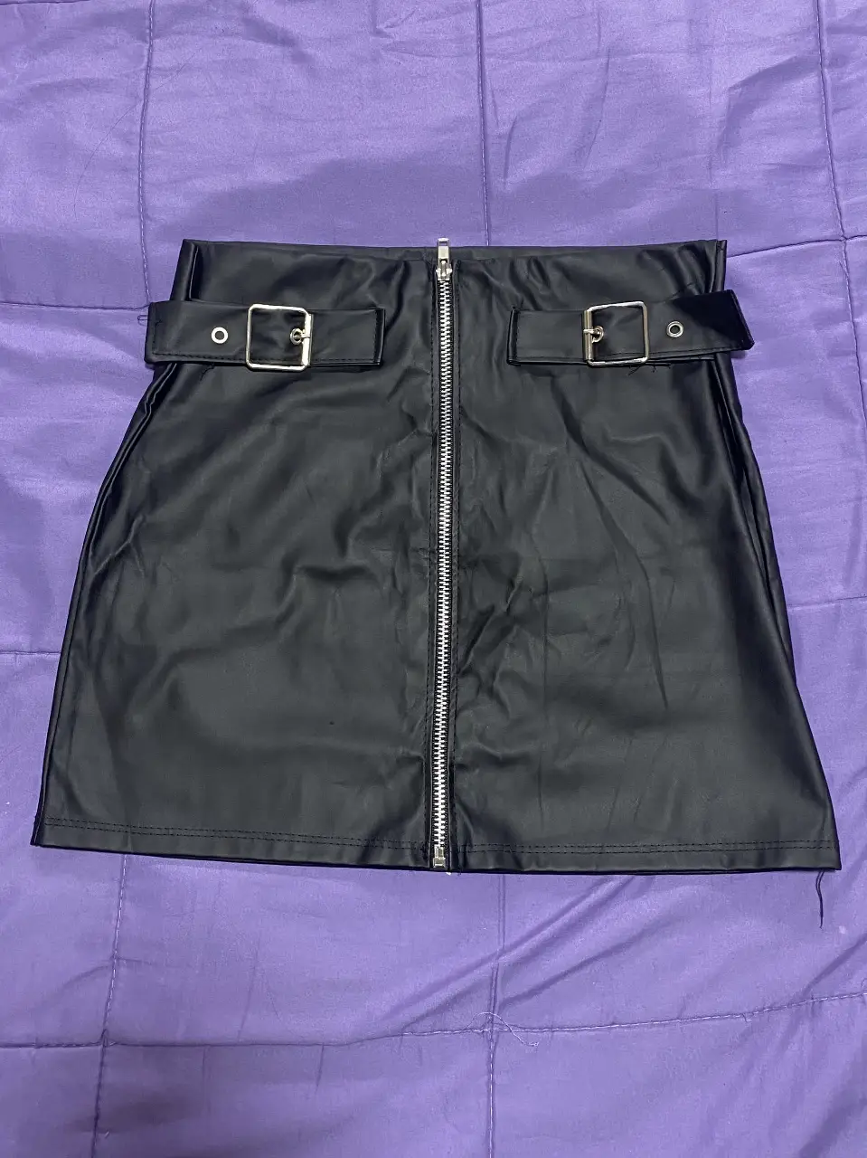 Minifalda de cuero sintético negra con cierre frontal y detalles de hebillas en la cintura. Ideal para un look moderno y audaz.