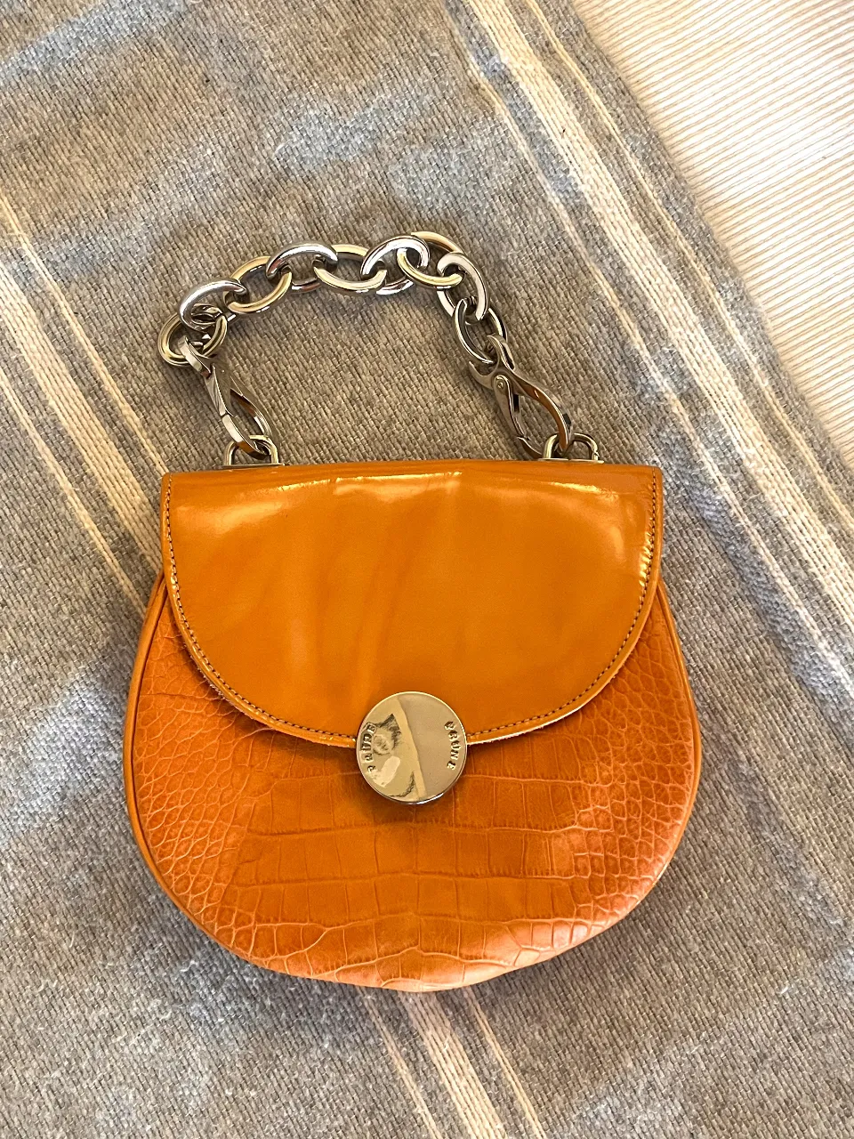 Cartera de mano naranja con textura de cocodrilo y cadena plateada. Interior de cuero. Marca Prüne.