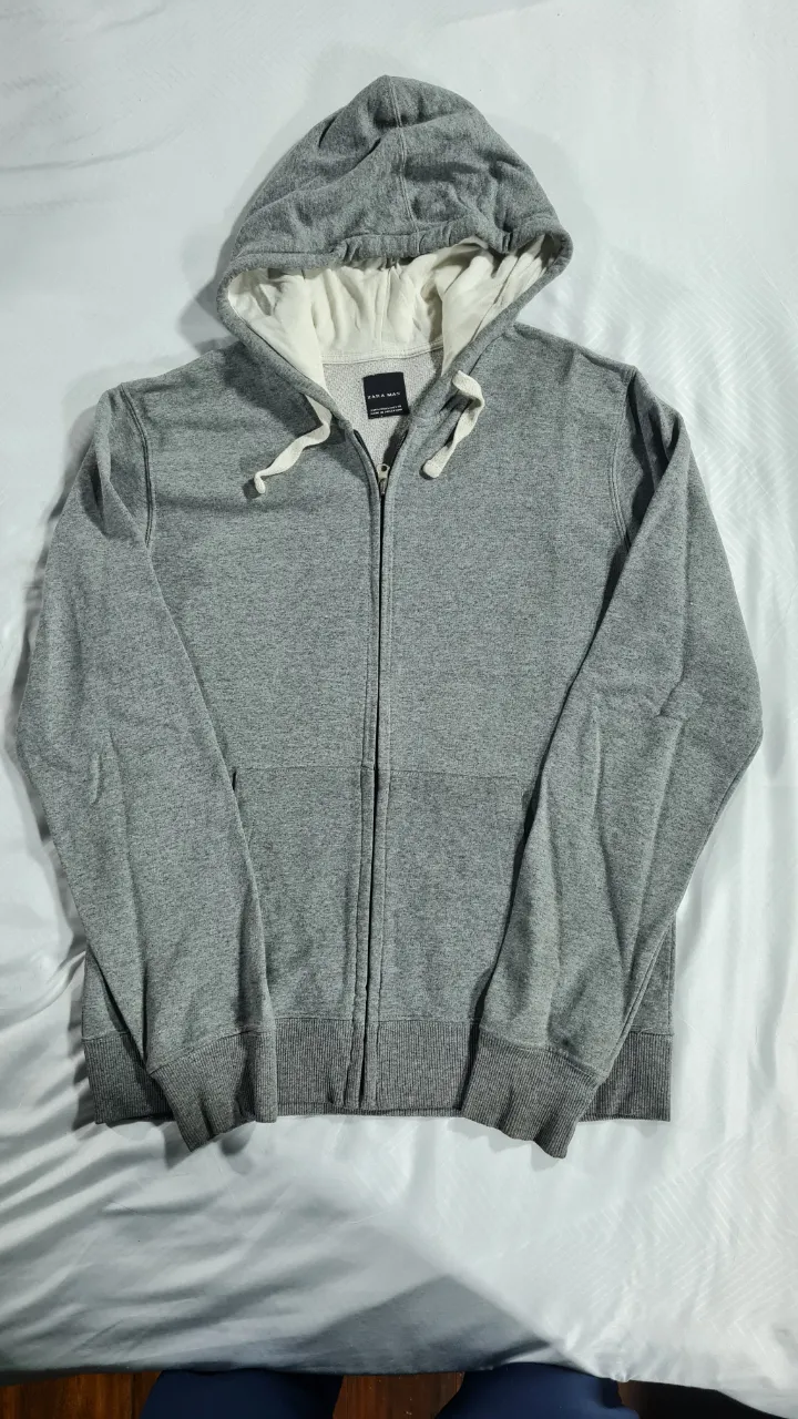Buzo con cierre para hombre, de color gris, con capucha y etiqueta de la marca Zara Man. Ideal para un look casual y cómodo.