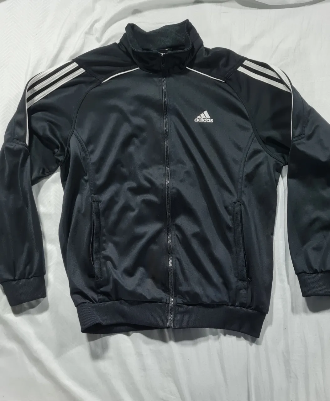 Campera deportiva Adidas negra con cierre y detalles blancos. Ideal para entrenar o usar en el día a día. Talle S.